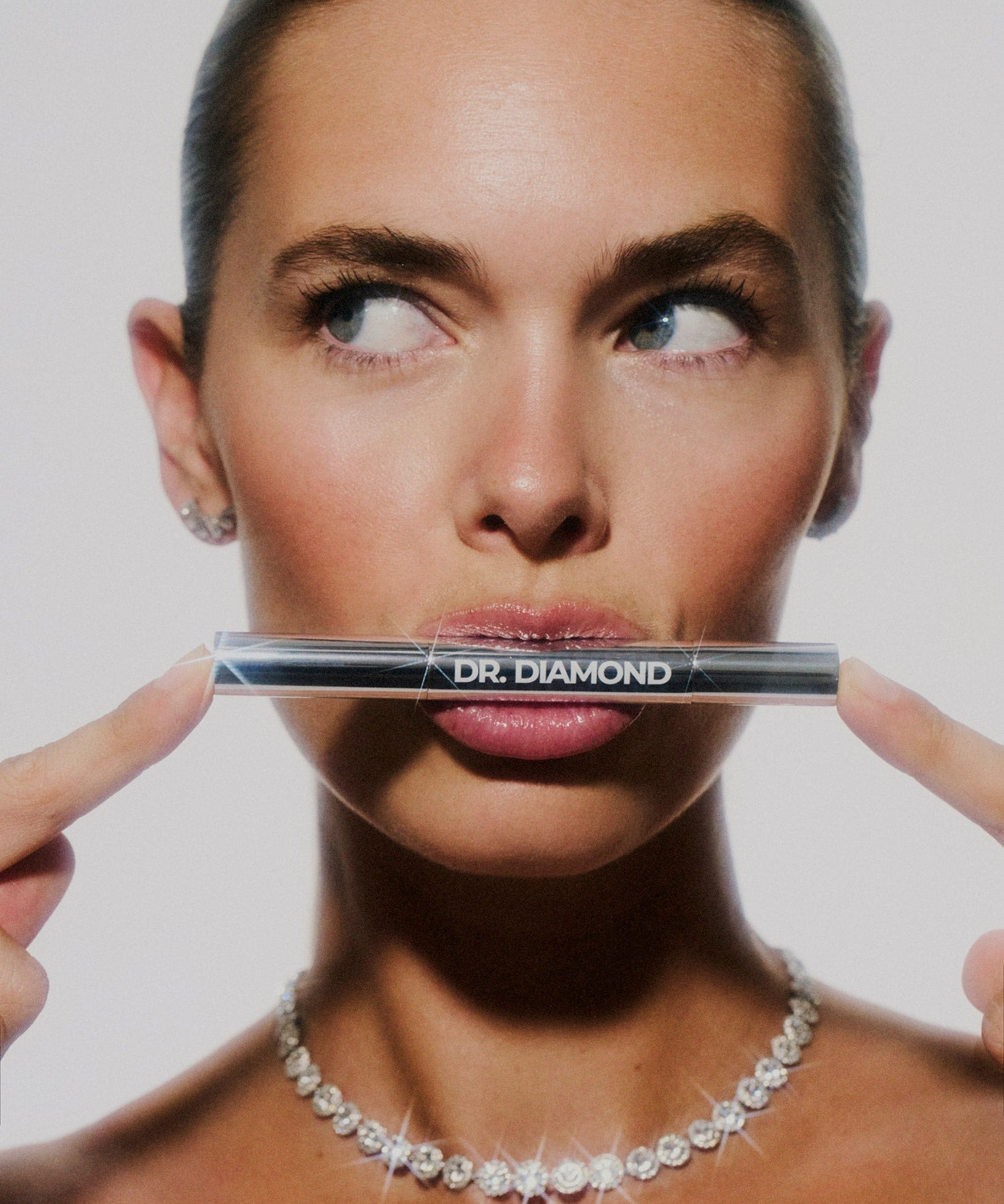 Woman holding Dr. Diamond jewellery cleaning pen in front of her face against a plain background