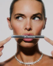 Woman holding Dr. Diamond jewellery cleaning pen in front of her face against a plain background