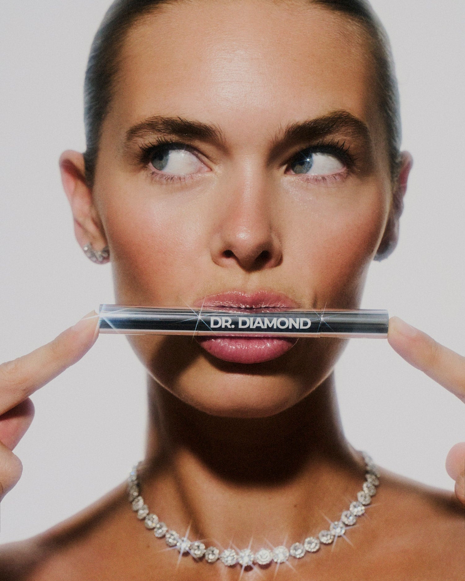 Woman holding Dr. Diamond jewellery cleaning pen in front of her face against a plain background
